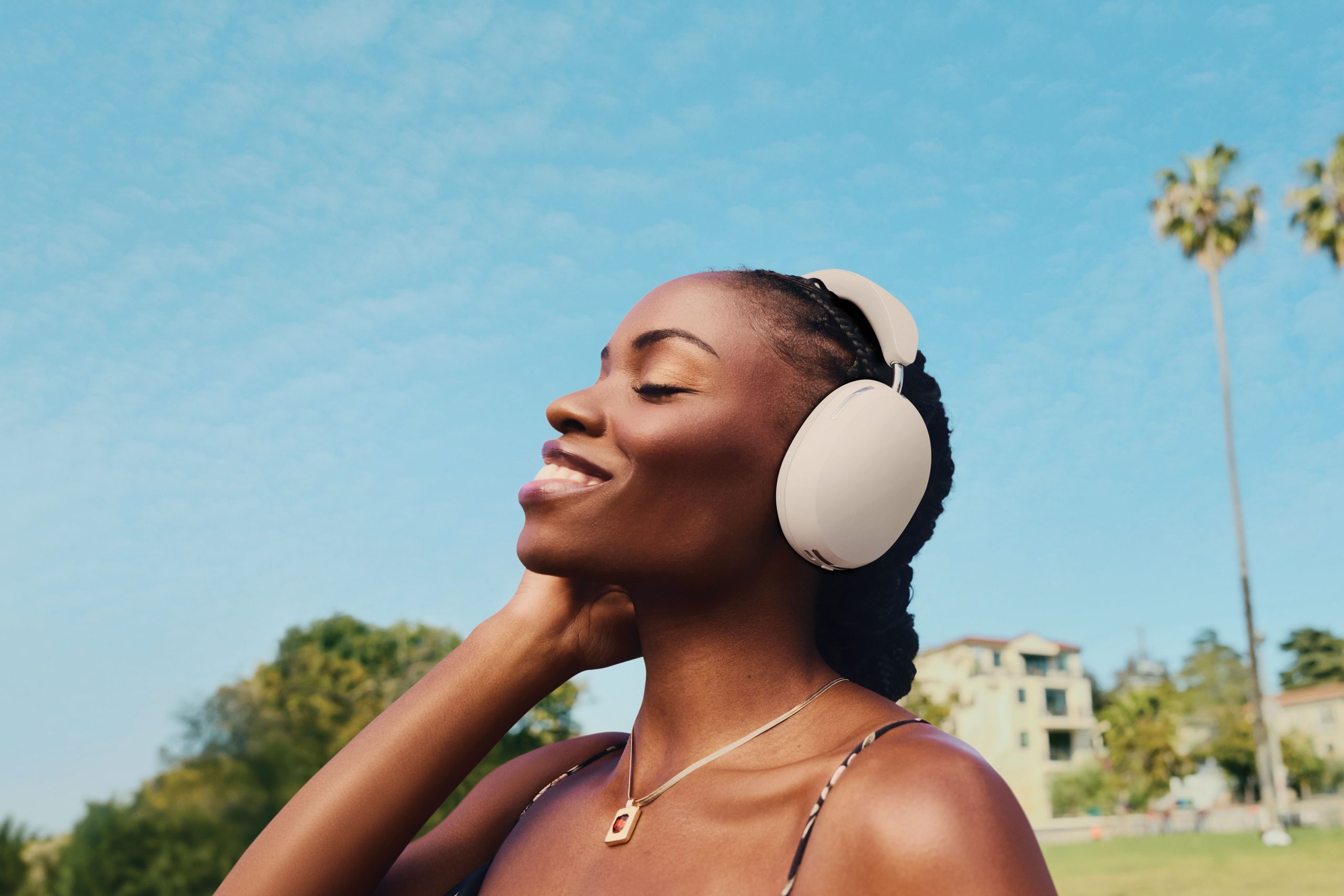 Person outside listening to music on white Sonos Ace headphones with blue sky and palm trees